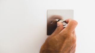 Silver dimmer switch being turned by hand to avoid flickering lights in house