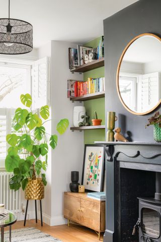 Bookcase in green alcove in living room, with oversized monstera in gold planter with legs