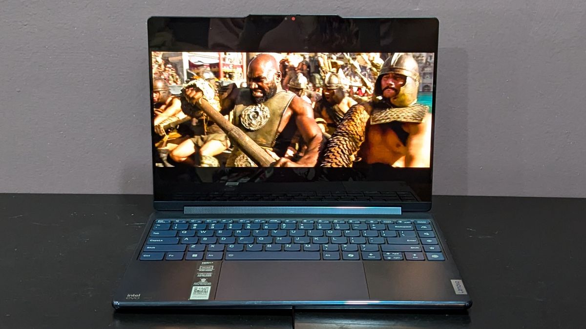 A straight-on view of an open and powered-on laptop on top of a black surface, showing a scene from a movie on its screen