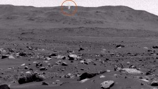 A black and white image of the surface of Mars with a small twister on the horizon (circled)