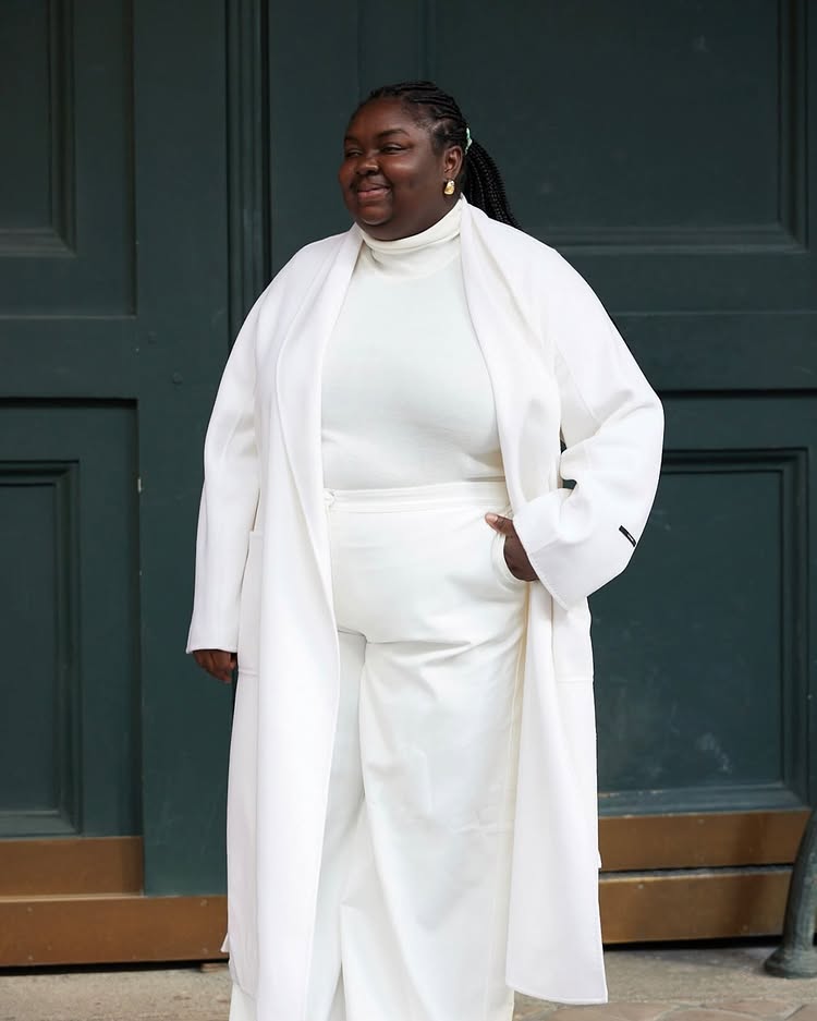 @abimarvel wears a cream thin roll neck jumper with a cream coat and trousers