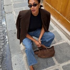Woman in wide-leg jeans, a brown blazer, and a suede bag