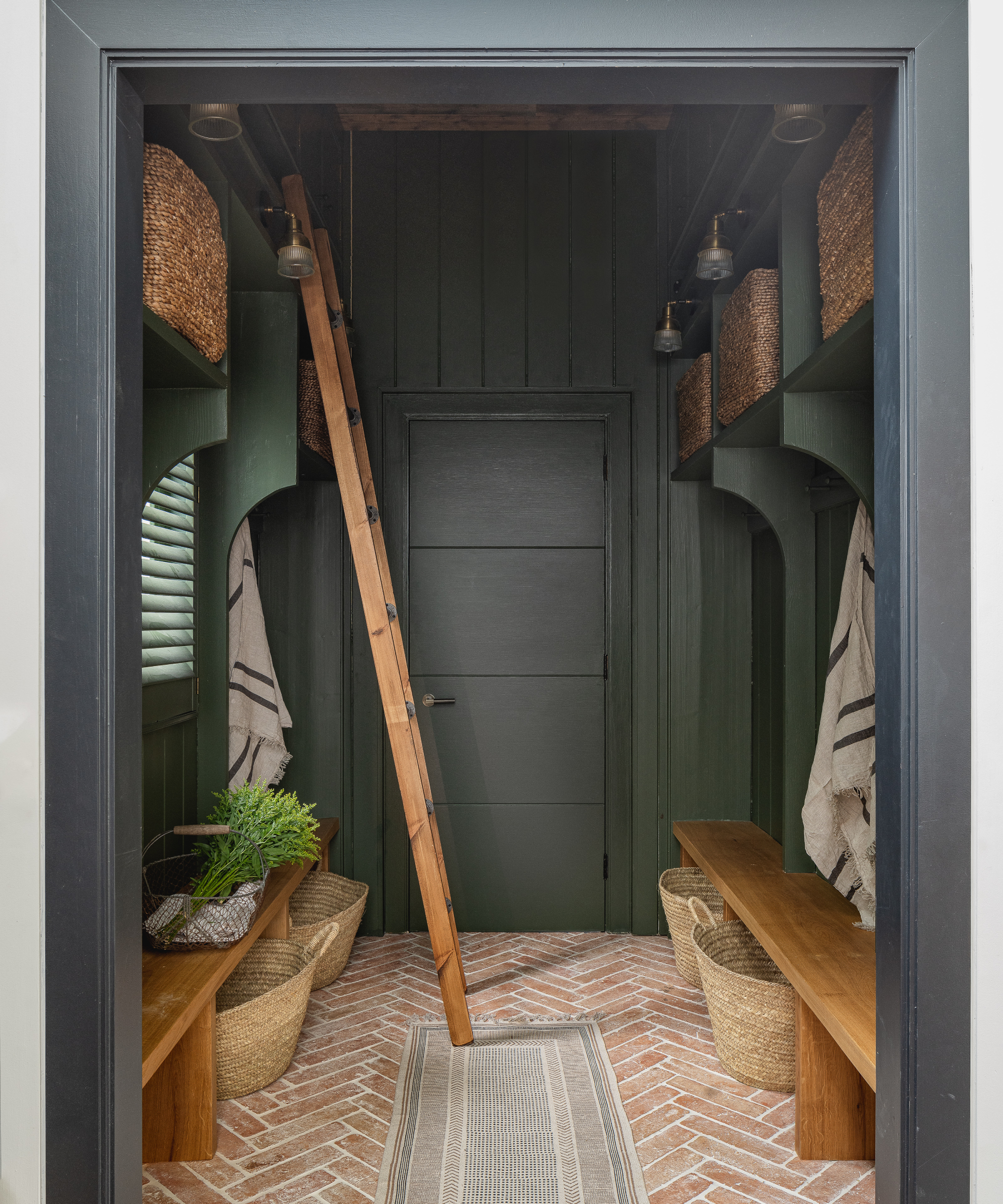 boot room painted in dark grey with herringbone brick tiled floor, wooden seating and ladder to reach high storage shelves