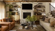 a relaxed farmhouse style family room with arched alcove storage, vintage ceiling beams, neutral couches, fireplace, armchairs and layered foliage