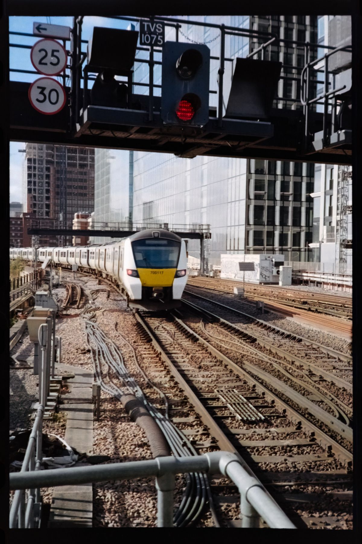 Scanned film photograph of a commuter train approaching along multiple railway tracks beneath signal lights and speed-limit signs.
