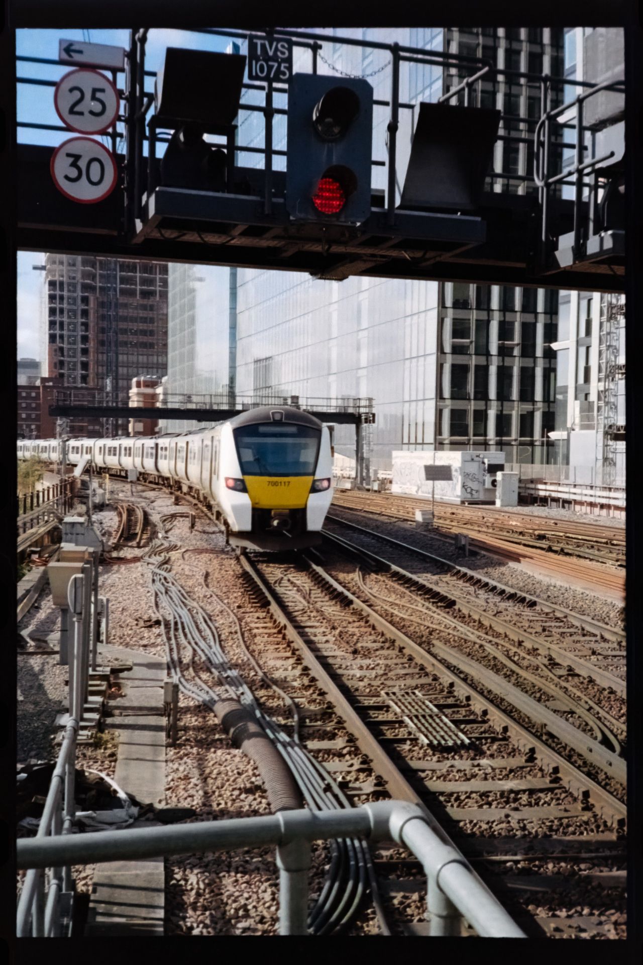 Scanned film photograph of a commuter train approaching along multiple railway tracks beneath signal lights and speed-limit signs.