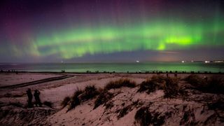 Northern lights (aurora borealis) illuminate the sky as visitors walk along Hornbaek Beach in the northern part of Sealand, Denmark late on February 27, 2023.
