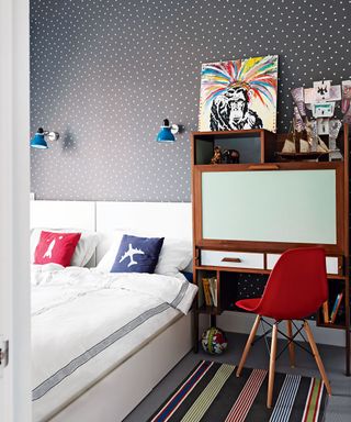 Black wallpaper with white spots, red, white and blue accents and a storage desk illustrating how to design clever bedrooms for kids.