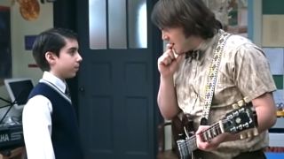 Jack Black holding a guitar and talking to a student in School of Rock