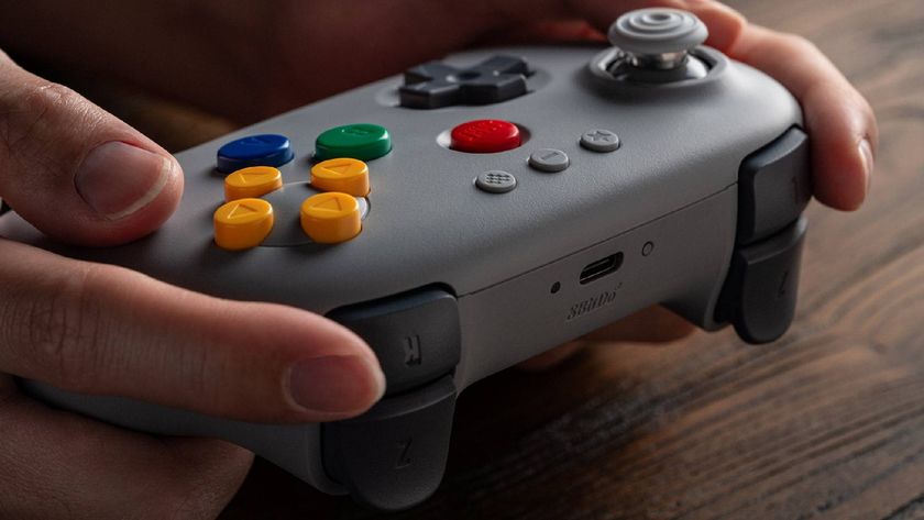 Hands holding 8Bitdo N64 controller in gray resting on woodgrain desk.