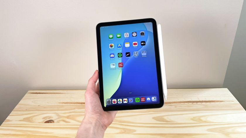 A hand holding up the iPad Mini 7 with Apple Pencil Pro attached in front of a wood table