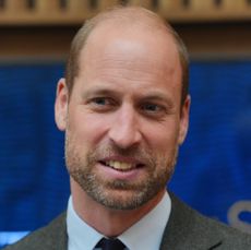 Prince William wearing a gray suit and tie smiling in front of a blue background