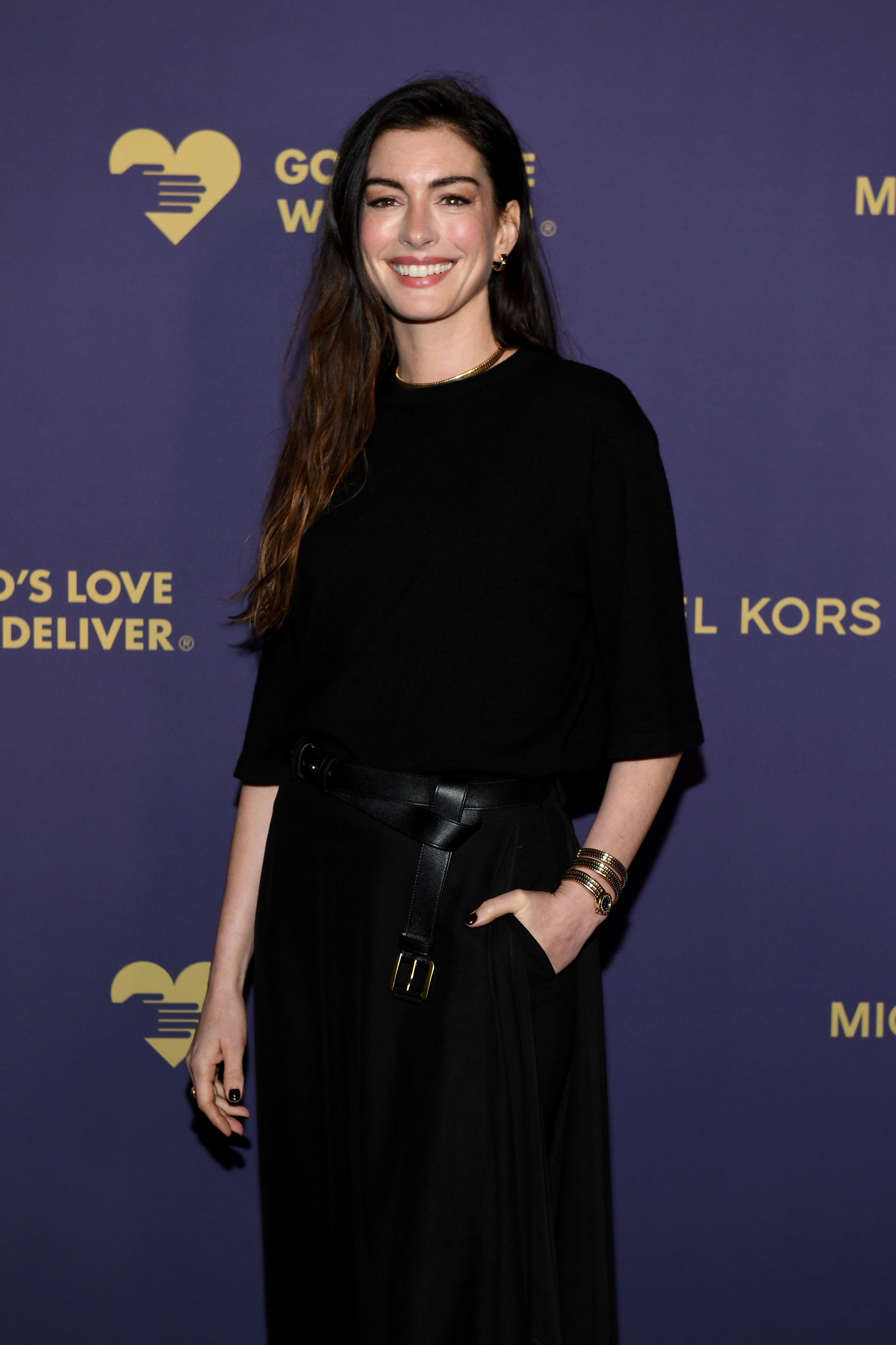 Anne Hathaway wearing wavy hair, deep red nails, and a black Michael Kors outfit.