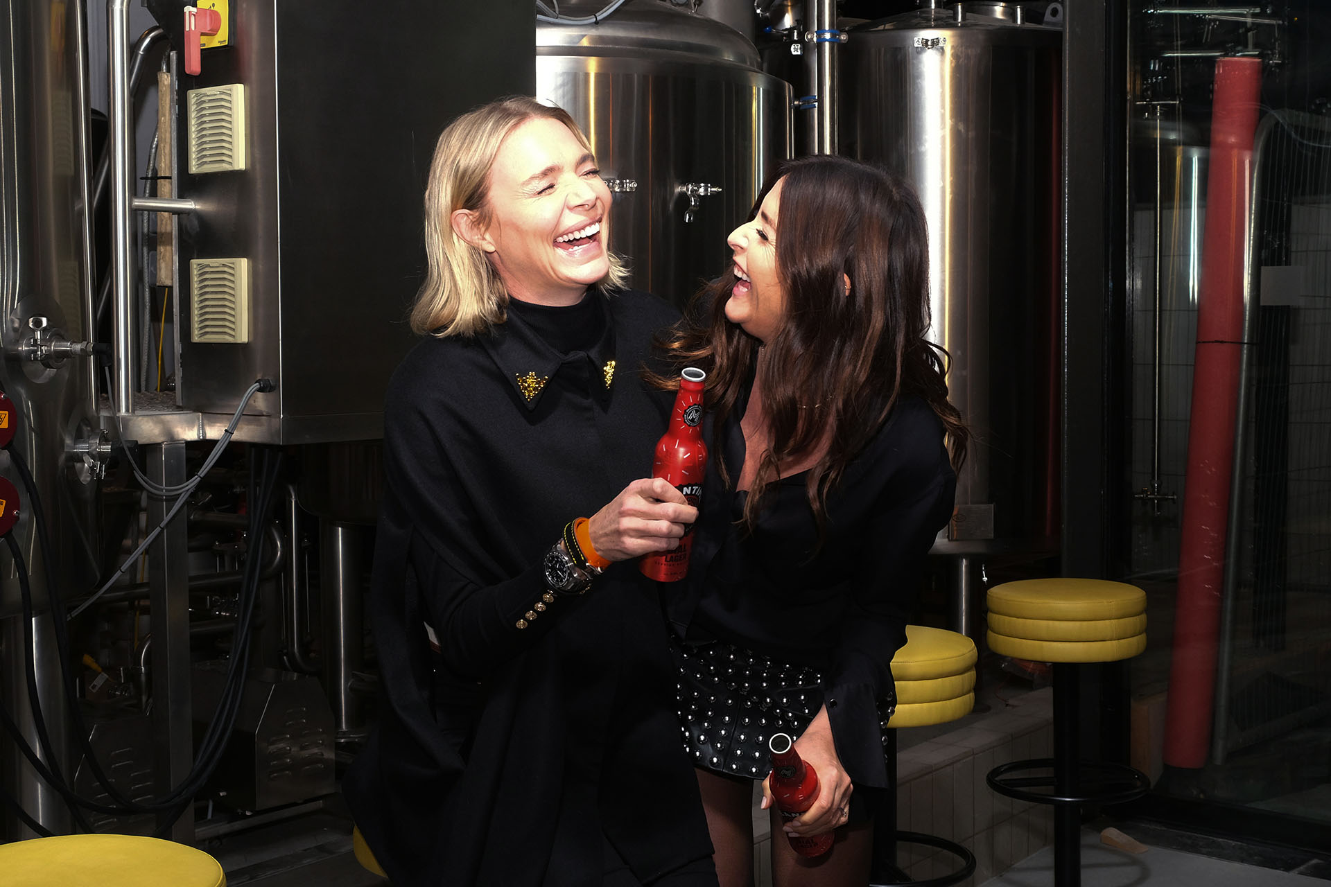 Two women in front of brewing equipment.