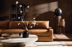 A brown leather sofa with a wooden coffee table and vase with flowery branch