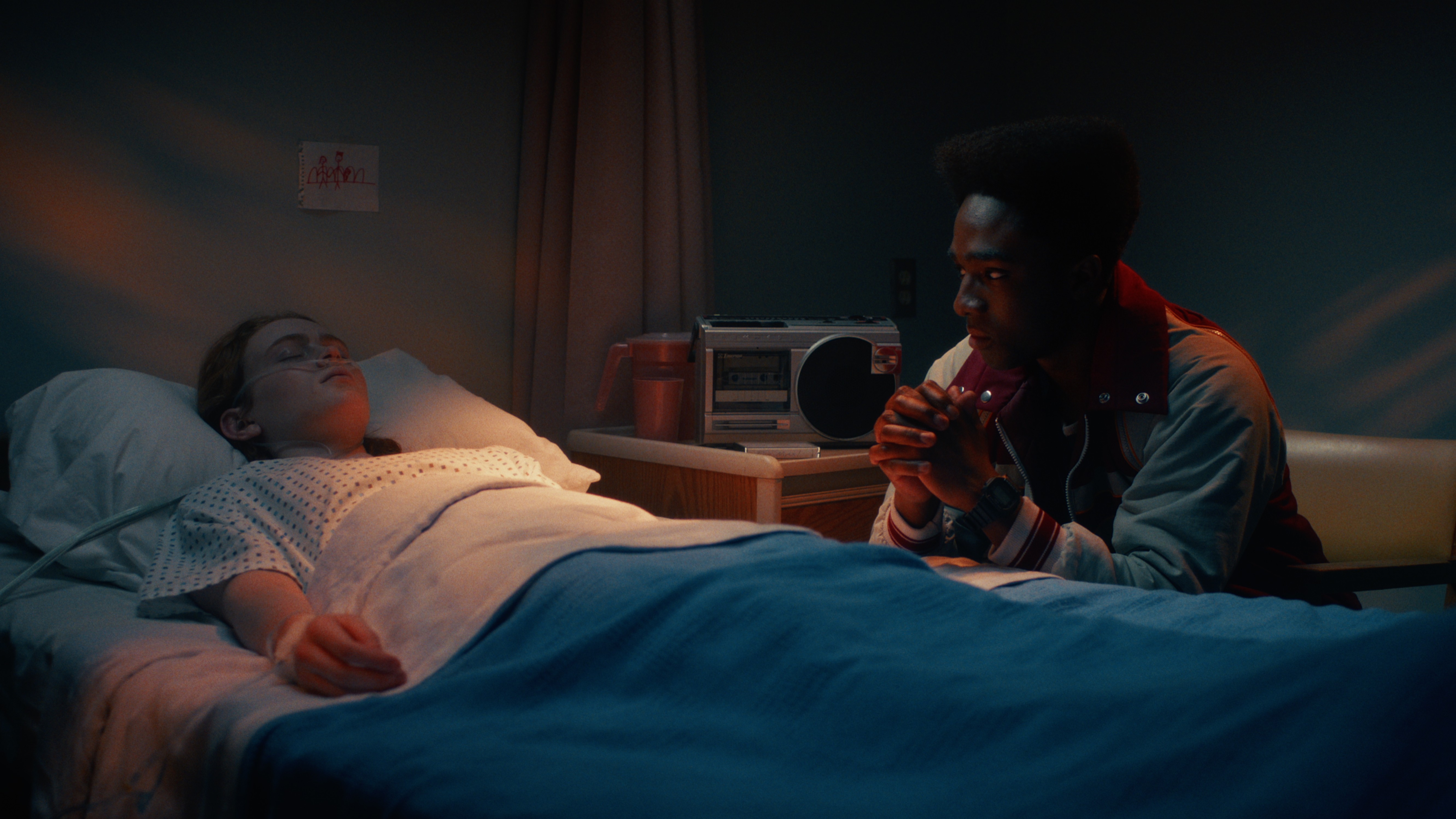 L-R: Max (Sadie Sink) lies in a hospital bed, with Lucas (Caleb McLaughlin) sitting by her side in a scene from Netflix's "Stranger Things" season 5