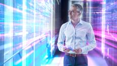 Digital transformation concept image showing male technologist in casual work wear standing in an office with glowing walls of data on either side.