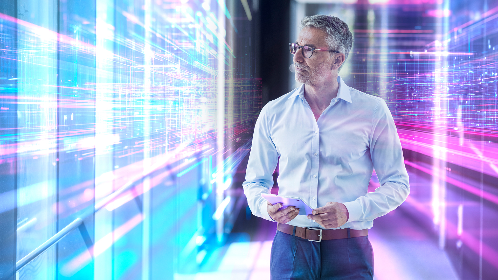 Digital transformation concept image showing male technologist in casual work wear standing in an office with glowing walls of data on either side.