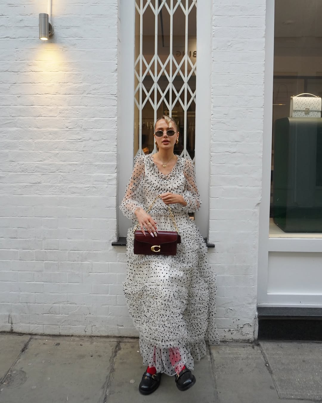 Influencer Evie Mills on a tulle polka dot dress black Mary Janes, pink socks and burgundy coach bag.