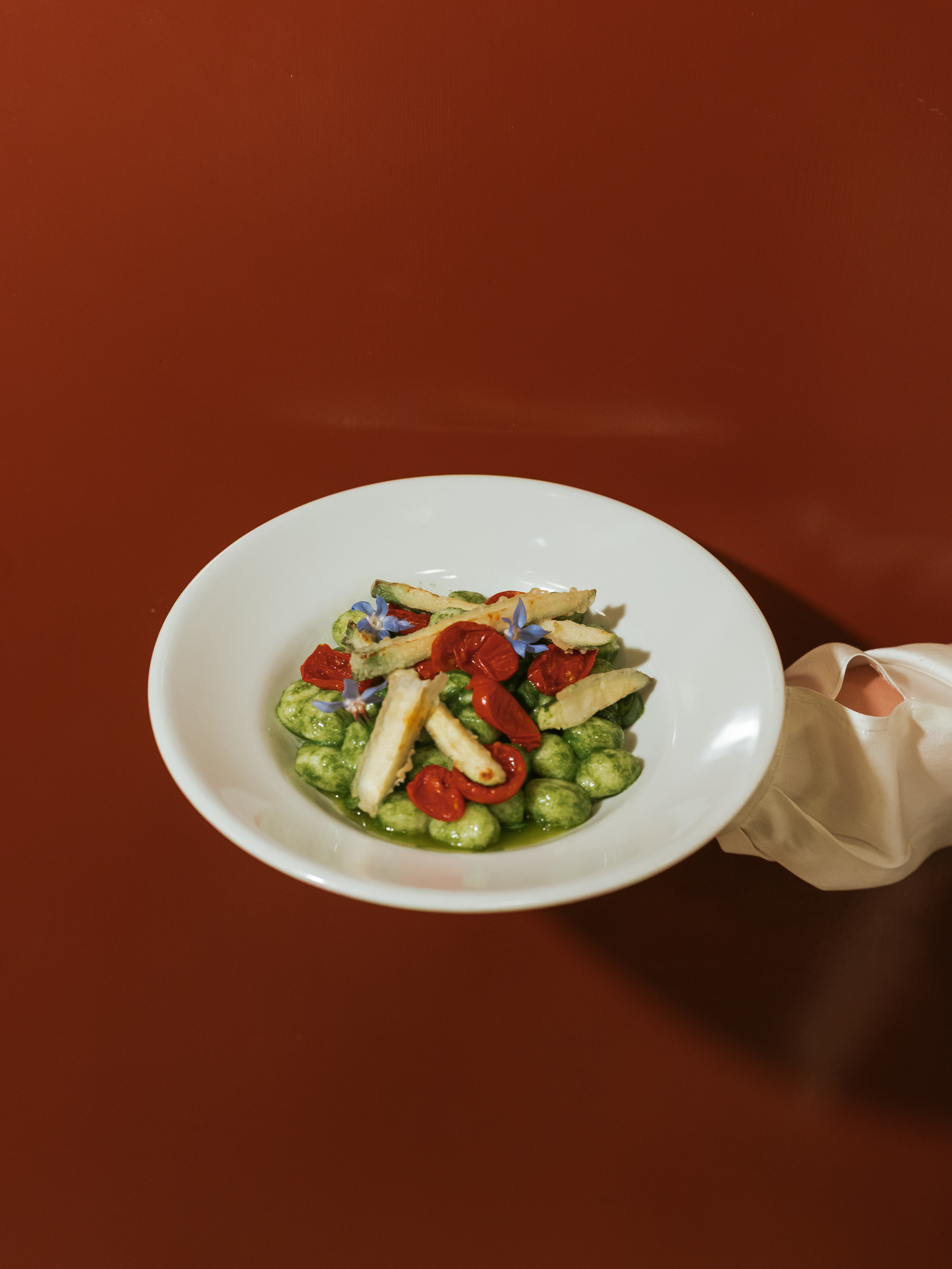 A retro-inspired restaurant&#039;s ambiance features coffered ceilings, a red, black, cream, and ochre palette, and mid-century leather, rattan, and chrome chairs, while simply delicious, vegetable-based plates reproduce the same colors.