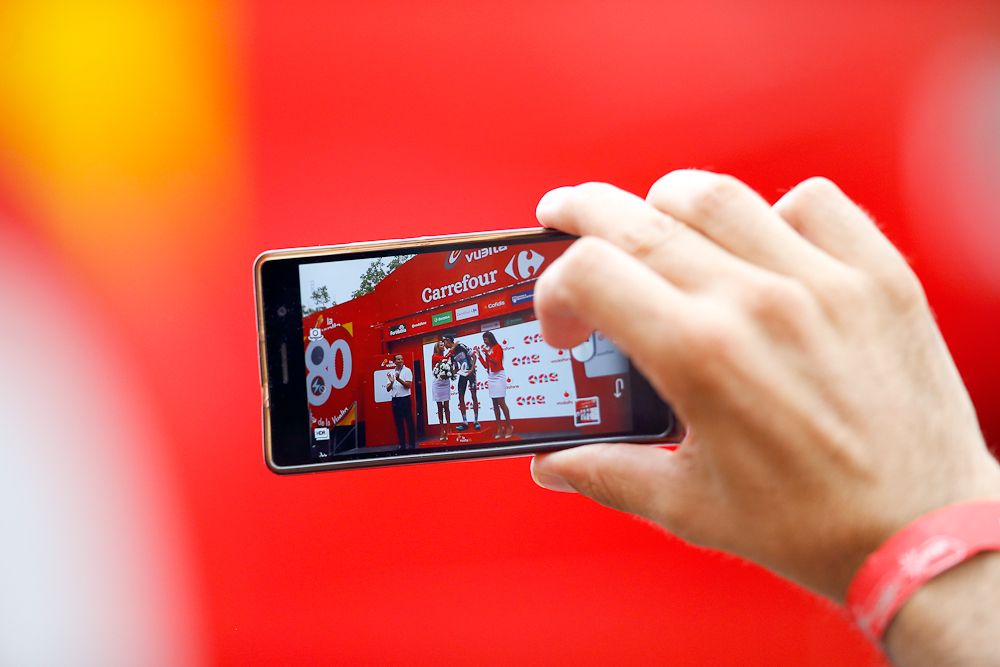 A fan captures the stage 10 podium presentation on a smart phone.