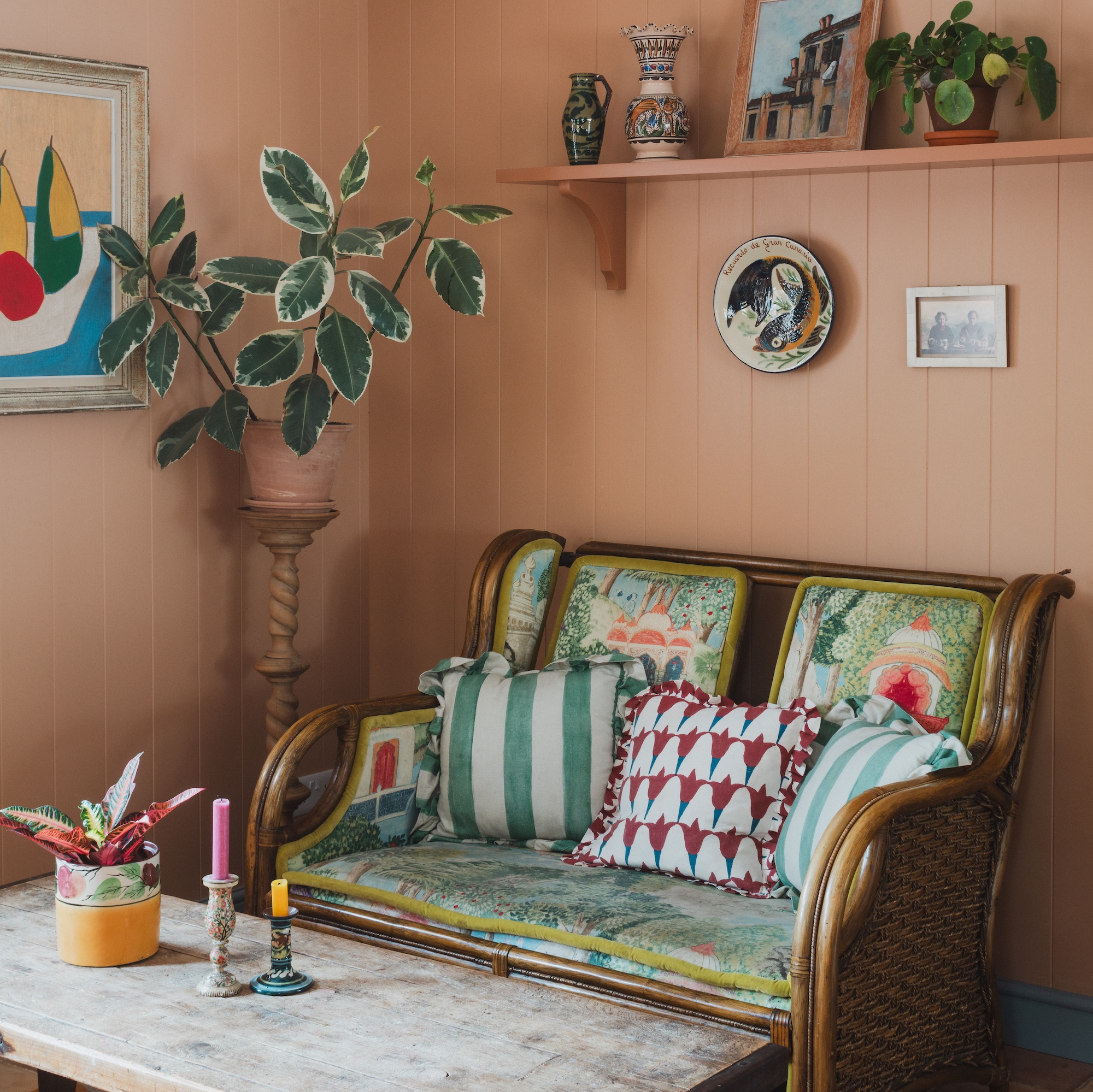 seating area with wooden wall panelling painted taupe terracotta, with small antique sofa with colourful cushions and coffee table