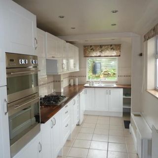 white galley kitchen with neutral floor tiles and window with blind