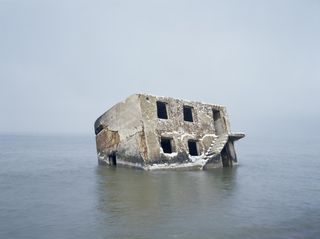 An abandoned Red Army bunker in Liepaja, Latvia, by Geert Goiris. A broken down building in the middle of a body of water.