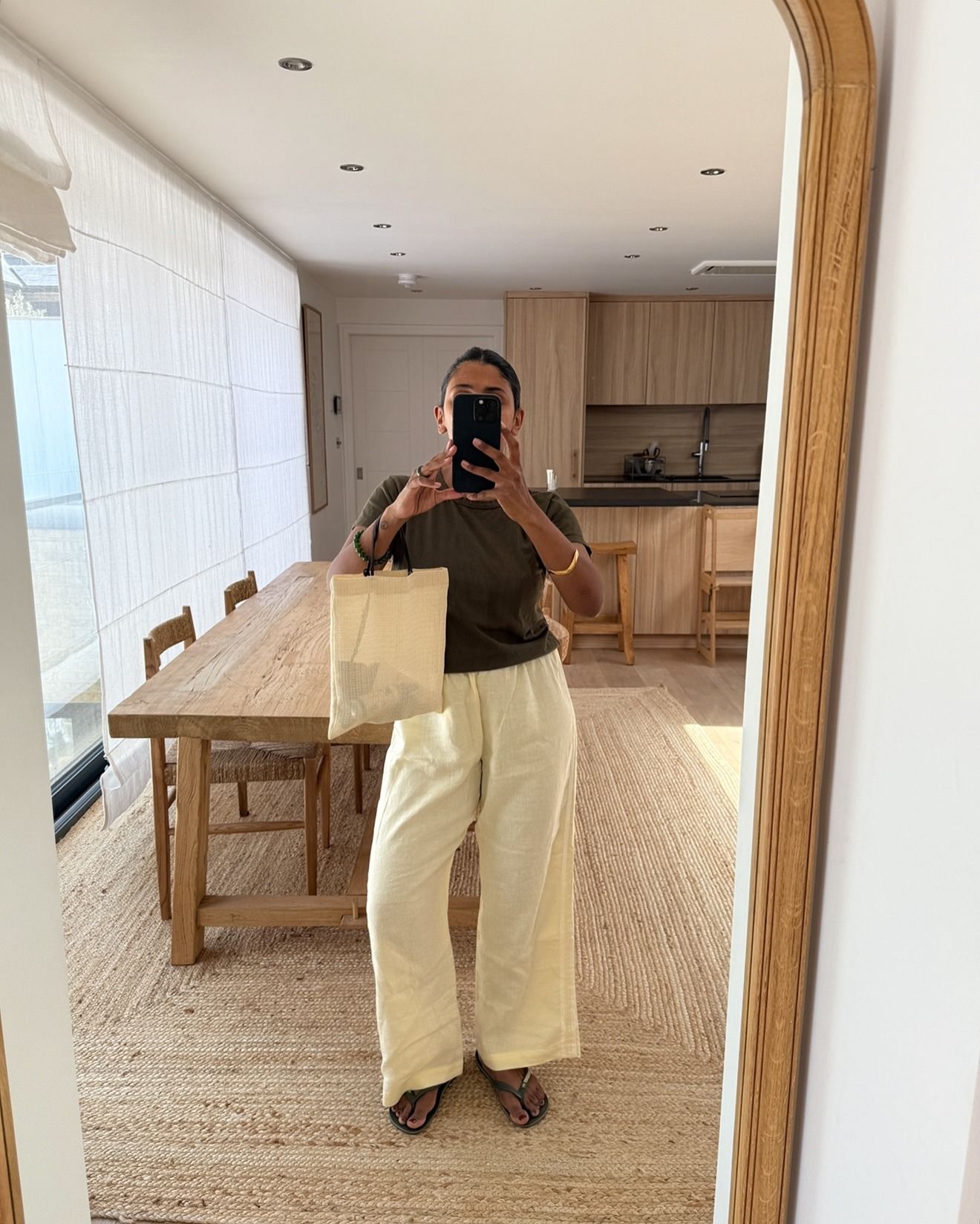 Influencer wearing linen pants, olive t-shirt, and beige The Row mesh market tote.