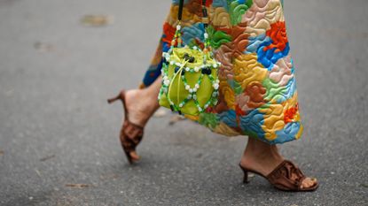 A guest a Copenhagen fashion week wears a multicoloured, quilted skirt, brown satin sandals and a brown pedicure colour