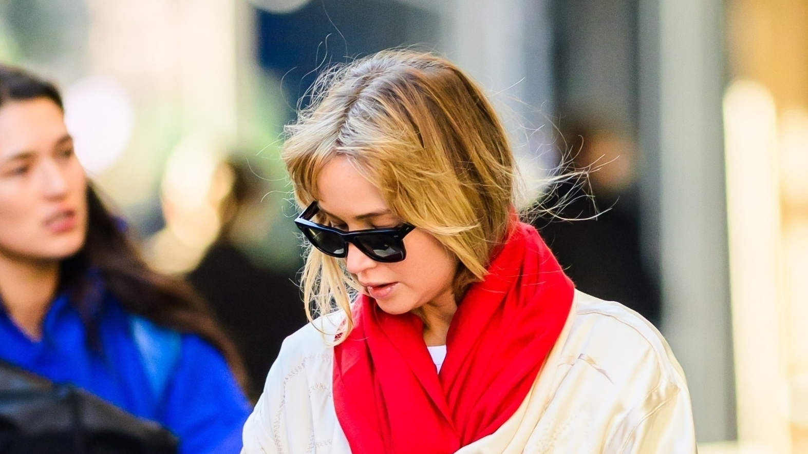 Jennifer Lawrence wearing a cream coat, red scarf, black pants, sneakers, and a Hermès Birkin bag in NYC