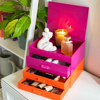 Colored makeup drawers stacked in orange and pink, with candle and sculptural figurine