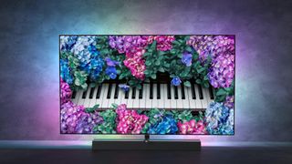 The Philips OLED+935 TV displaying a piano surrounding by blue, pink and purple flowers