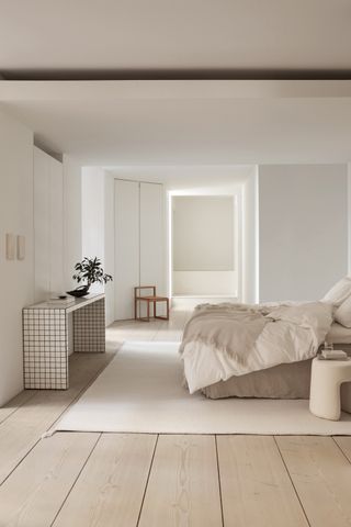 Large minimalist Scandi style bedroom, with white rug, white furnishings and soft furniture
