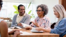 Four older adults smile and laugh during a book club meeting.
