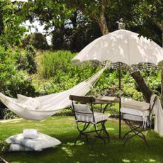 nglish country garden in summer, white cotton hammock, wrought iron and wood garden furniture, white vintage style parasol, floor cushions, large wicker basket full of apples.