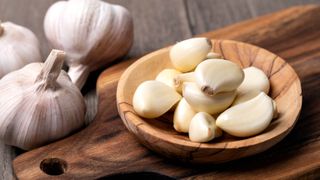 Several cloves of garlic in a bowl next to three bulbs of garlic