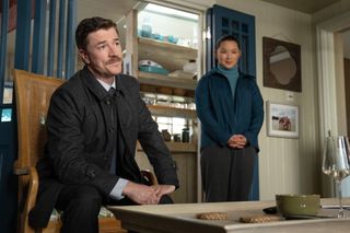 Barry Ward, sitting in a wooden chair, and Thaddea Graham, standing in a living room, in "Bad Sisters."