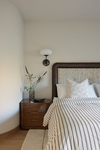 bedroom with cream walls, cream and brown bed, glossy wooden side table and flower display