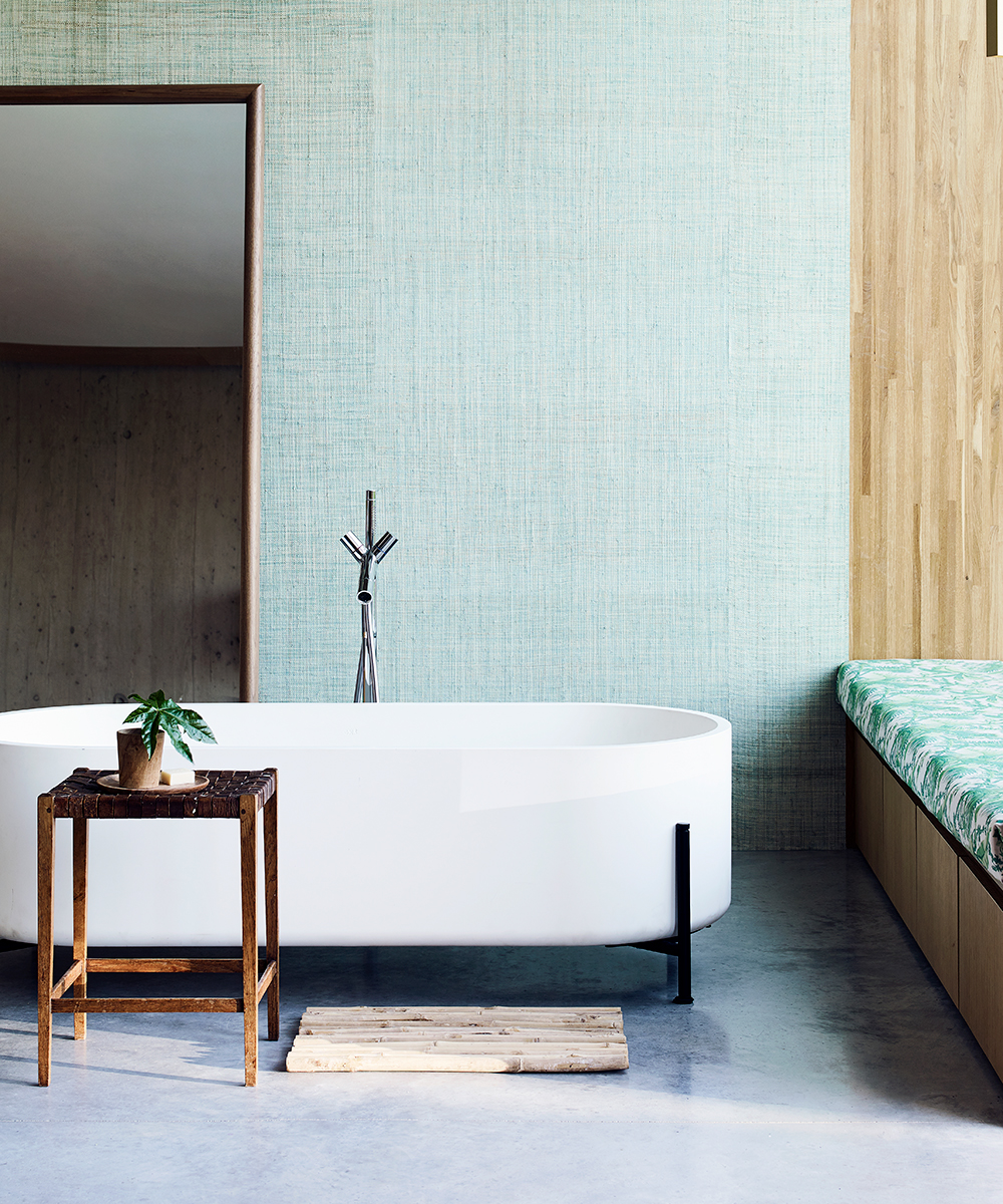 A white bath tub and green raffia wall as an example of the Japandi bathroom trend.