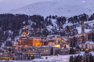 Buildings with lights illuminating the windows stand out against the snow on the St. Moritz mountain