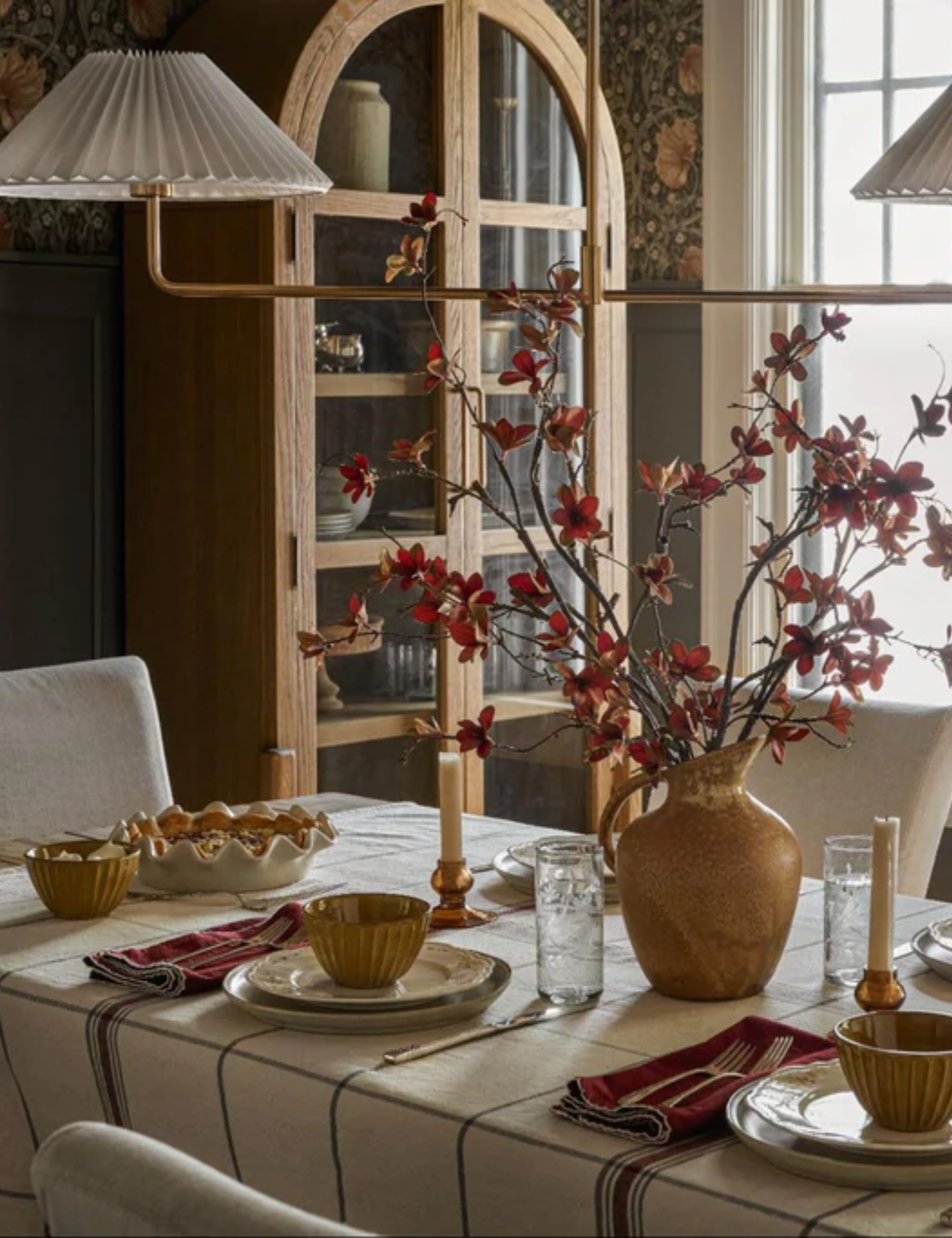 Spring tablescape featuring a cream-and-navy checkered tablecloth, an aged vase holding red floral branches, and eclectic tableware