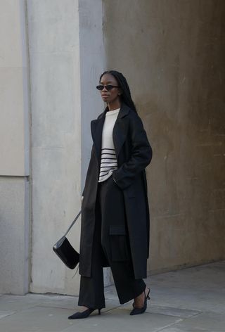 a photo showing what shoes to wear with wide-leg pants with a woman wearing a black trench coat over a black and white striped sweater styled with black wide-leg pants and black slingback heels