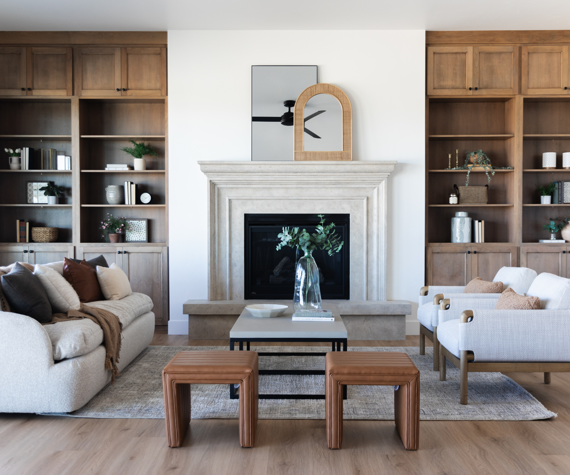 a formal living room with symmetrical design, a couch, two accent chairs, two stools, two built-in cabinets with decor, and a large fireplace in the center