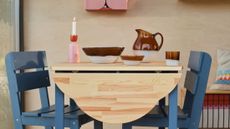 Blue and natural wood drop-lead dining table styled with a pink and red candlestick and blown-glass tableware.