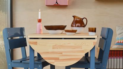 Blue and natural wood drop-lead dining table styled with a pink and red candlestick and blown-glass tableware.
