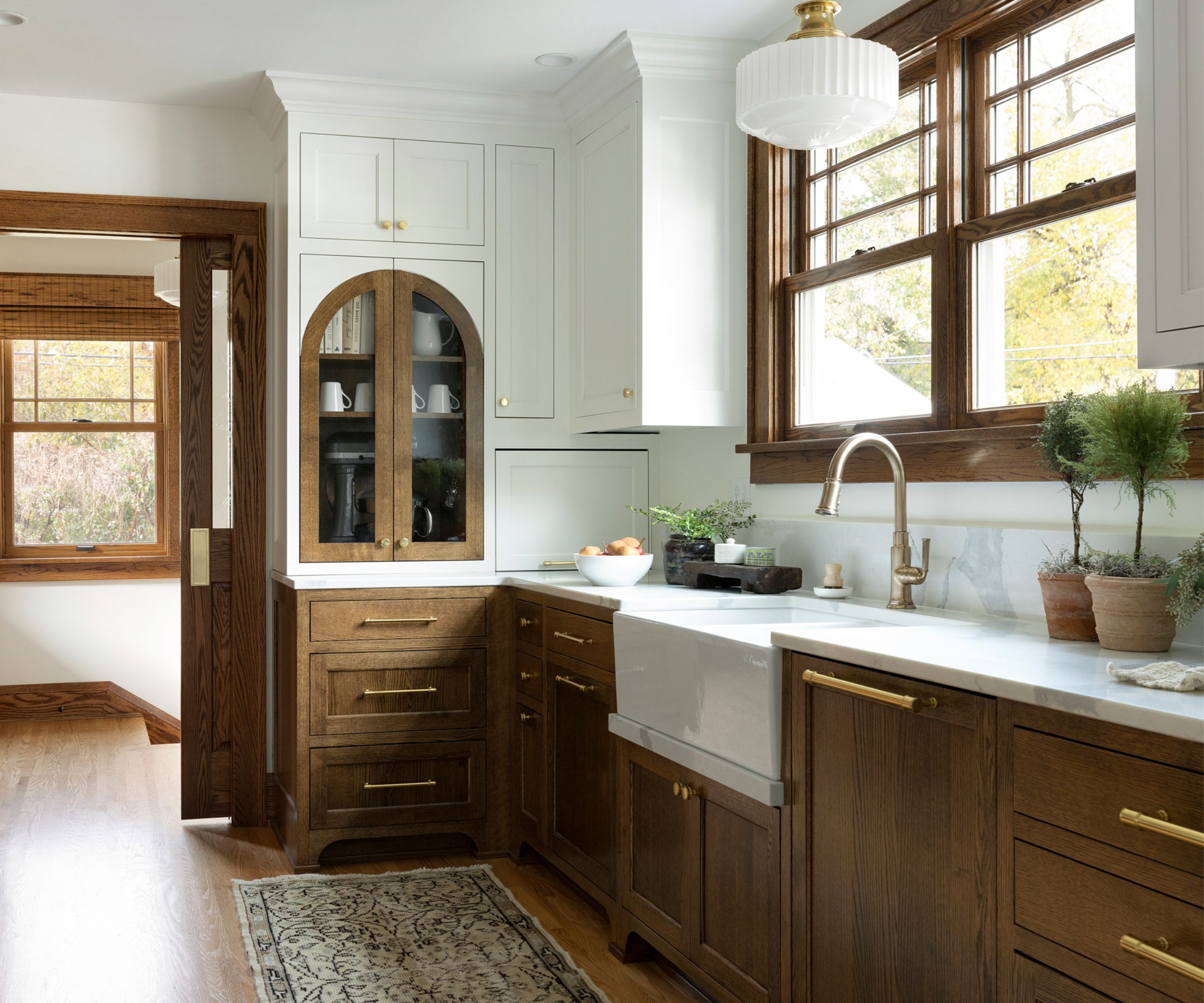 A small kitchen with wooden cabinets, white wall cabinets, and brass hardware