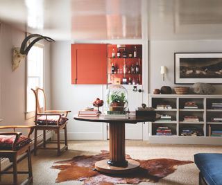 Hidden bar cupboard with dutch doors in a antique style living room with cow skin rug, wooden coffee table, books and wooden chairs