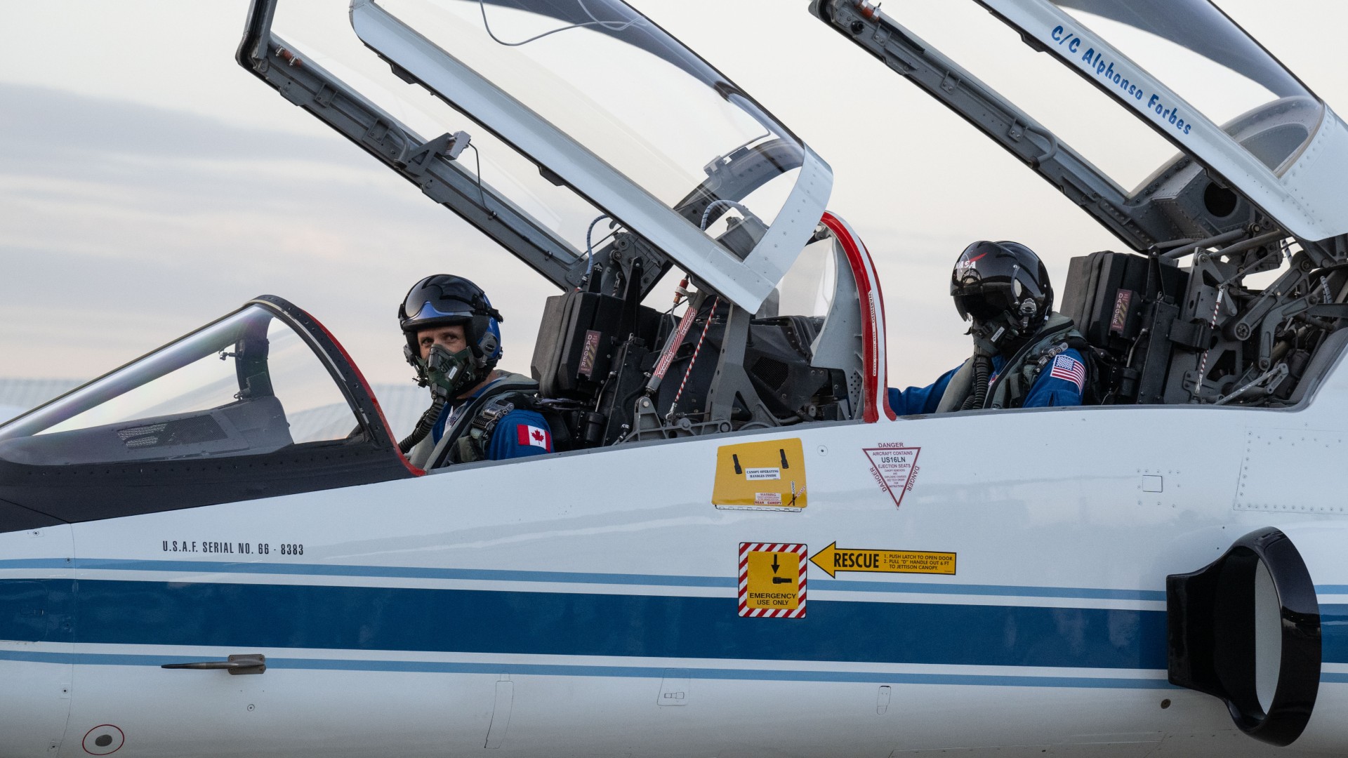 two pilots in the cockpit of a white jet on a runway