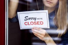 A store owner hangs a "sorry we're closed" sign on the door of her business.